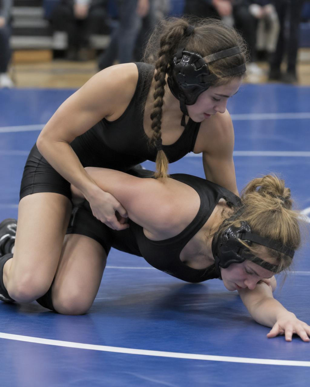 Two girls wrestling on a blue mat at a tournament
